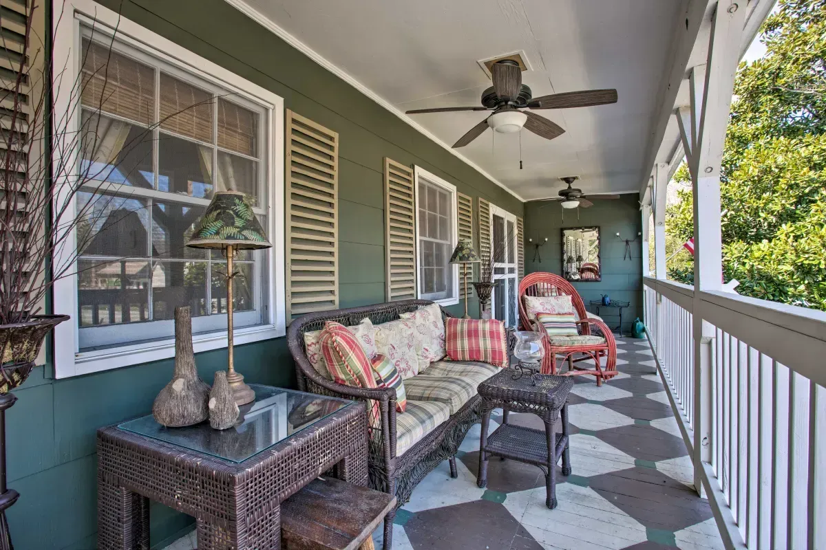 a porch with a couch , chairs , tables and a ceiling fan .