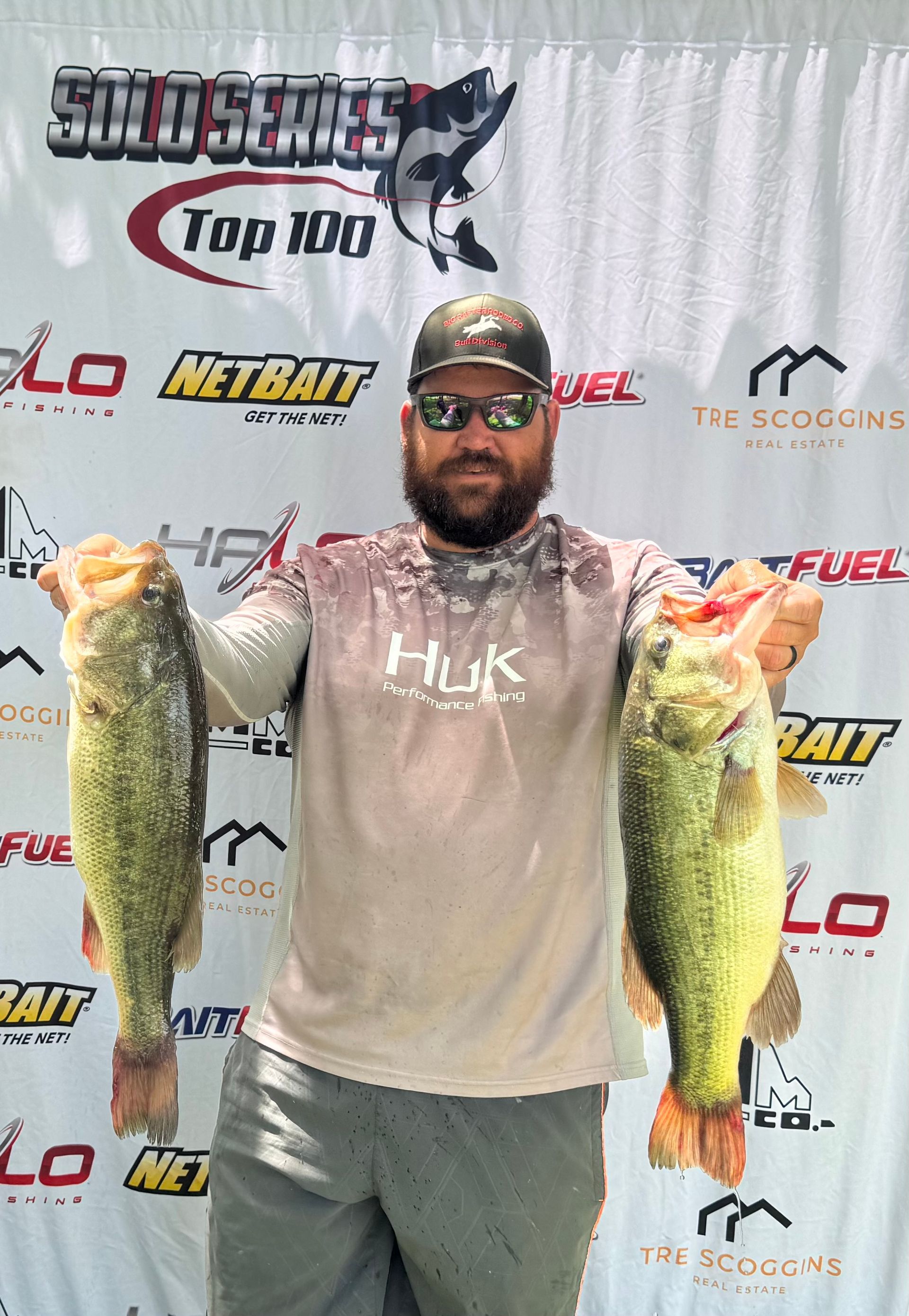 Angler posing with two large fish at a Top 100 fishing event backdrop.