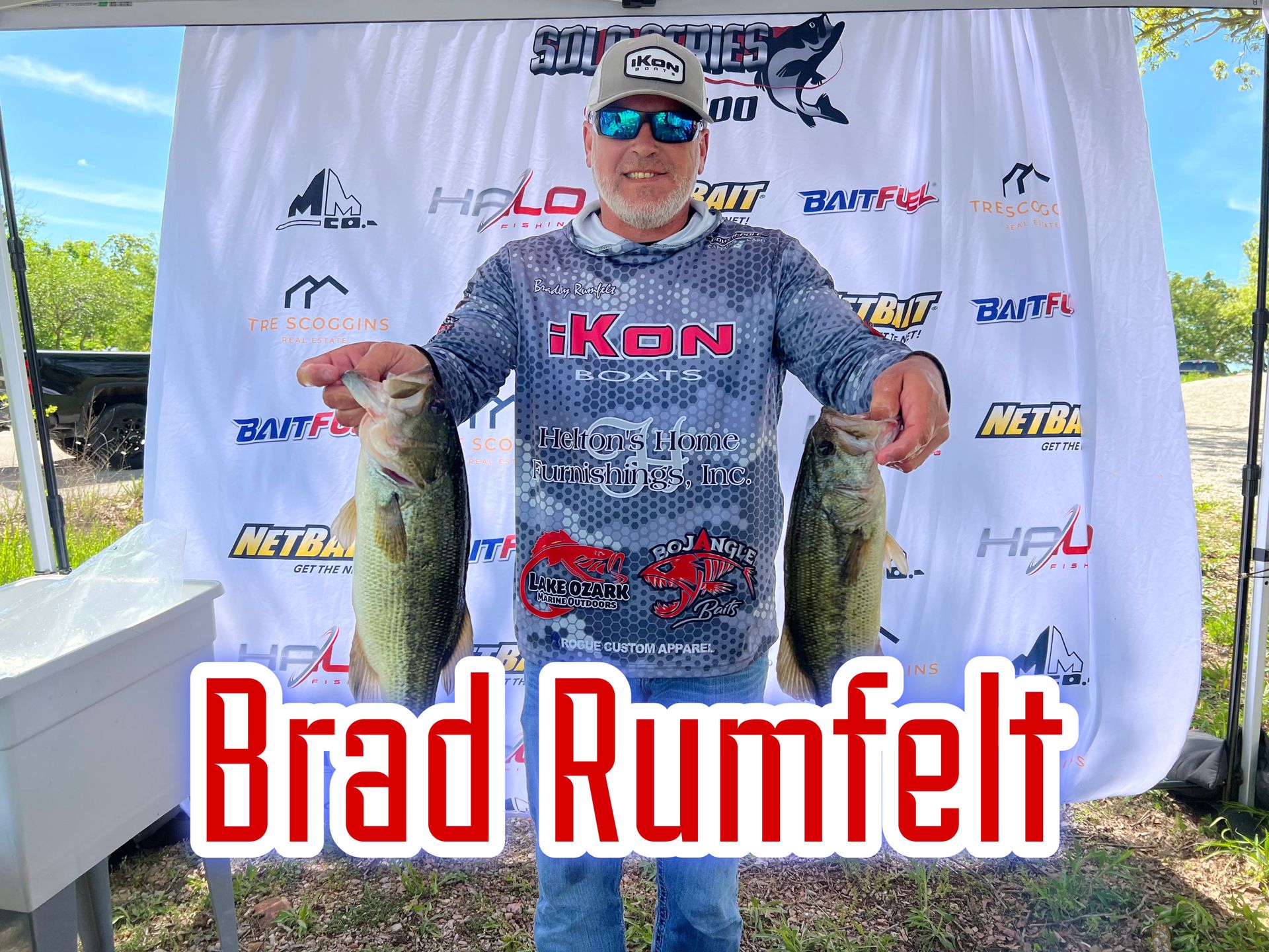 Angler holding two fish at a sponsor backdrop with “Brad Rumpf” text
