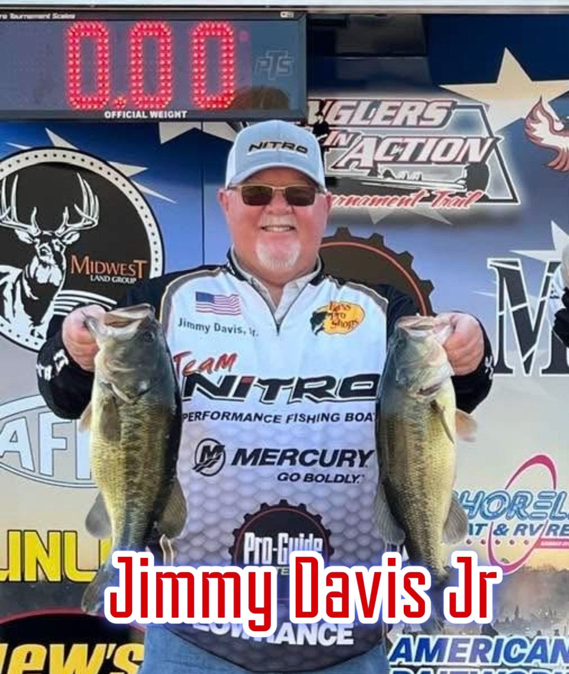 Man holding a large fish in front of a Bassmaster event backdrop and digital weigh-in display