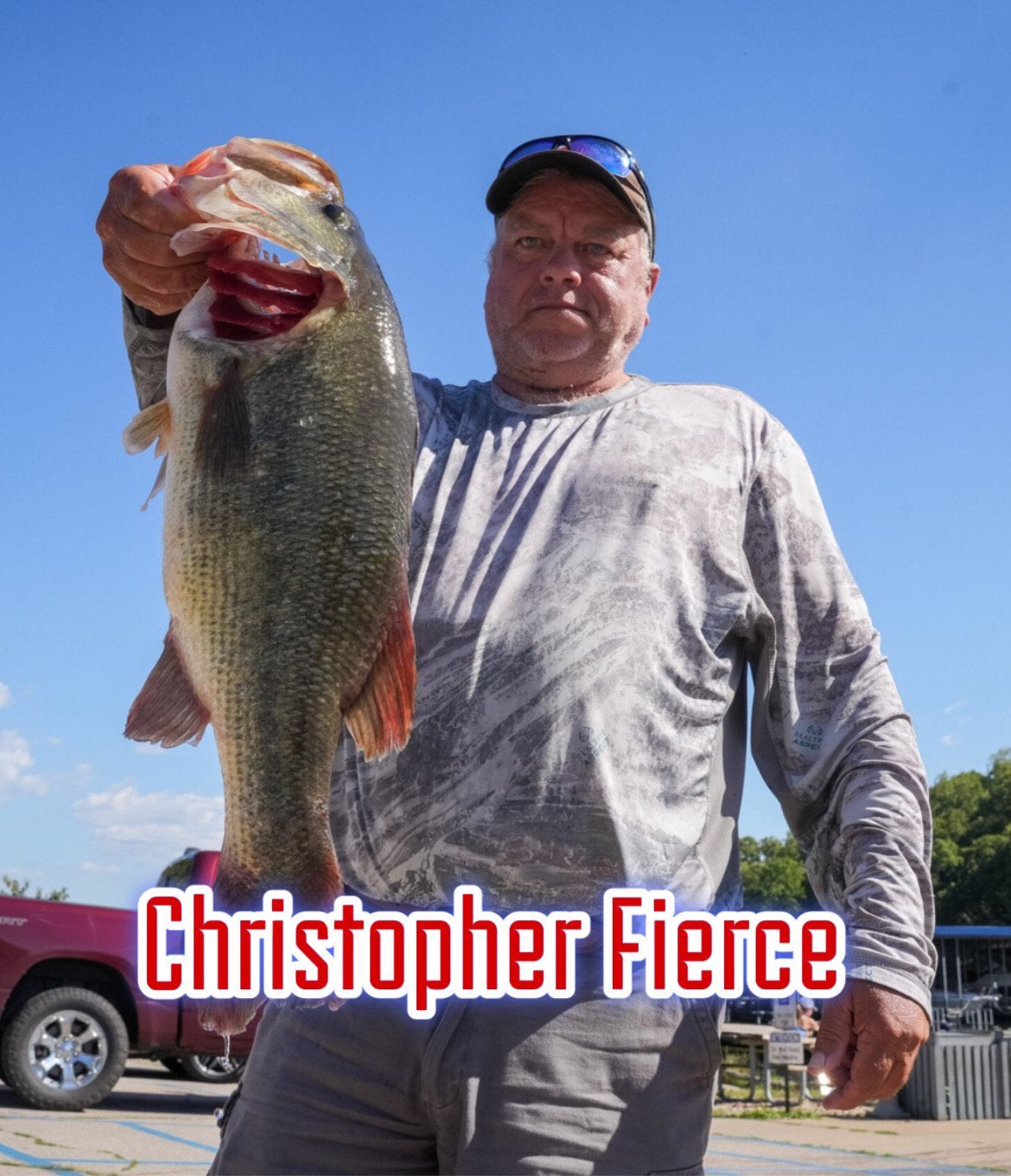 Man holding a large fish outdoors under a blue sky, with “Christopher Fierce” text at the bottom