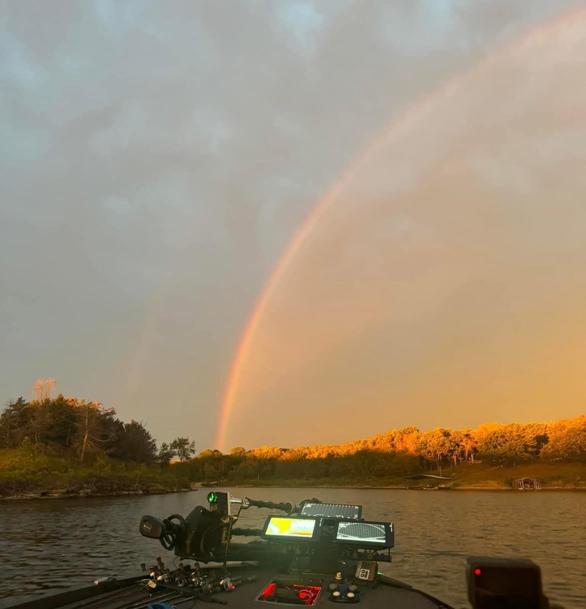 Rainbow over a river at sunset, viewed from a boat with camera gear in the foreground