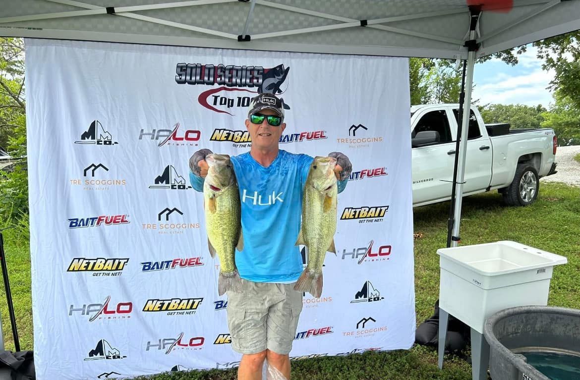 Angler posing under a canopy with two large fish at a fishing tournament backdrop