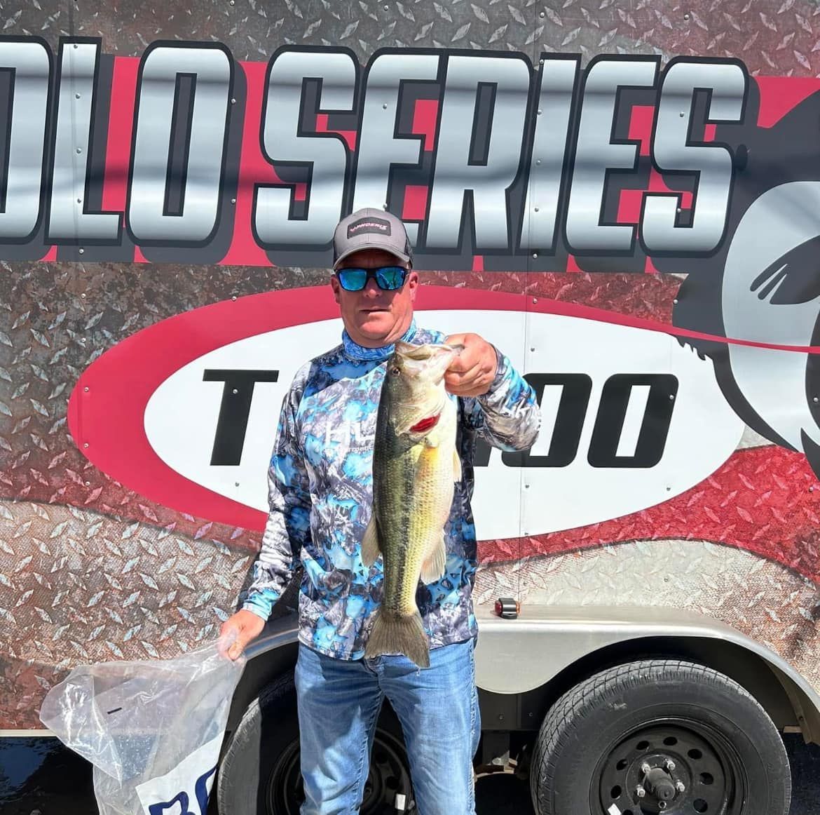 Angler holding a large bass in front of a Solo Series fishing trailer