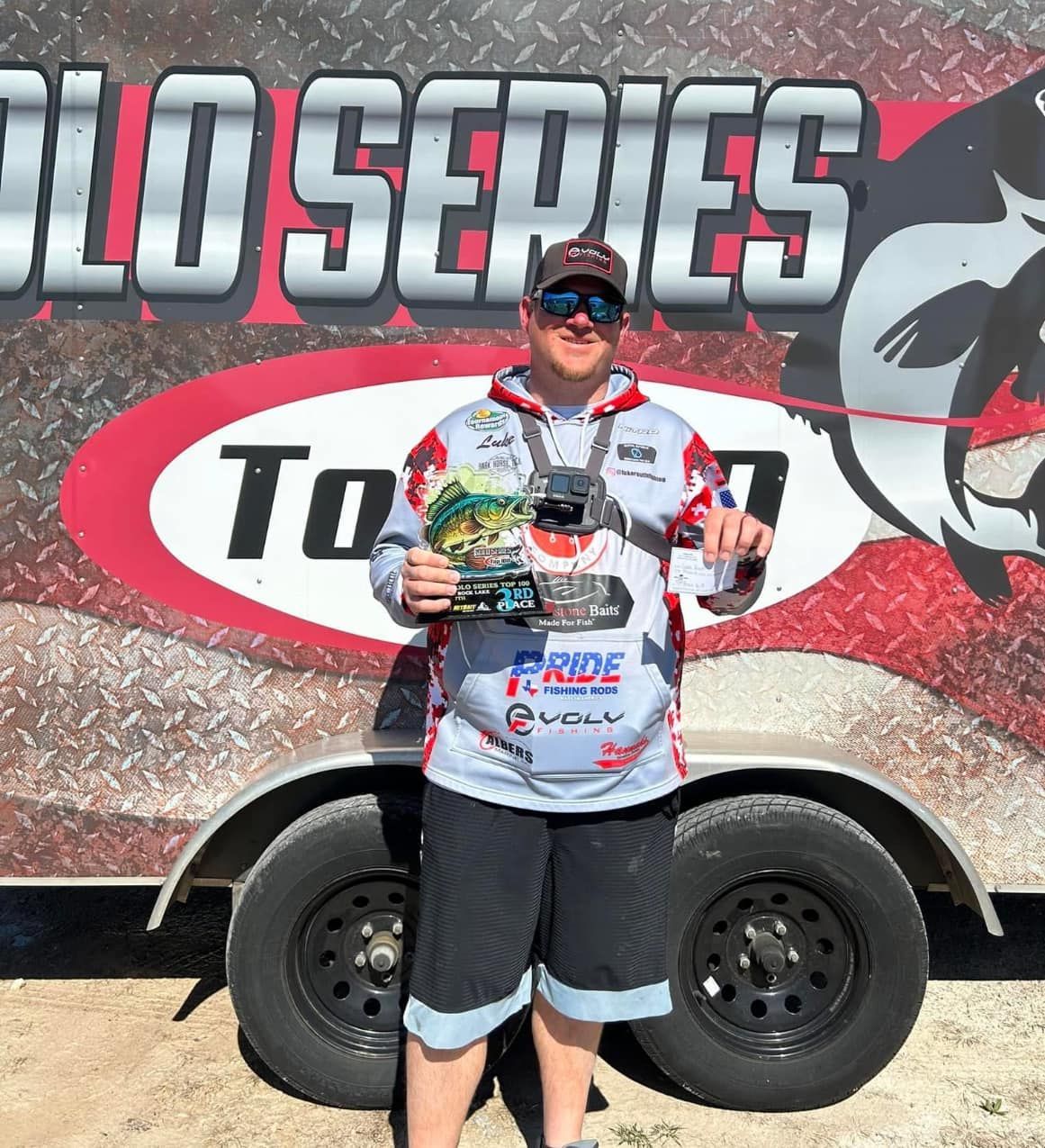 Race winner holding a trophy in front of a “Solo Series” trailer at an outdoor event