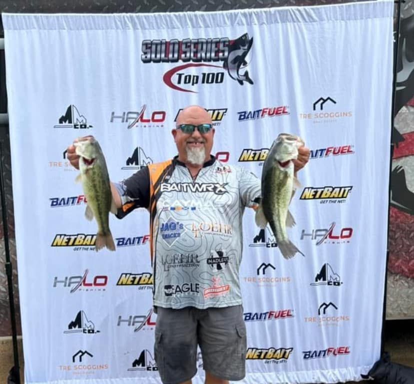 Man holding two large fish in front of a branded fishing tournament backdrop