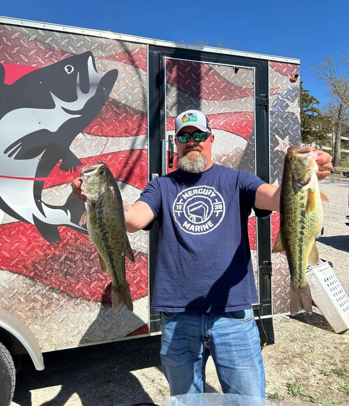 Man holding two large fish in front of a truck with a fish mural outdoors
