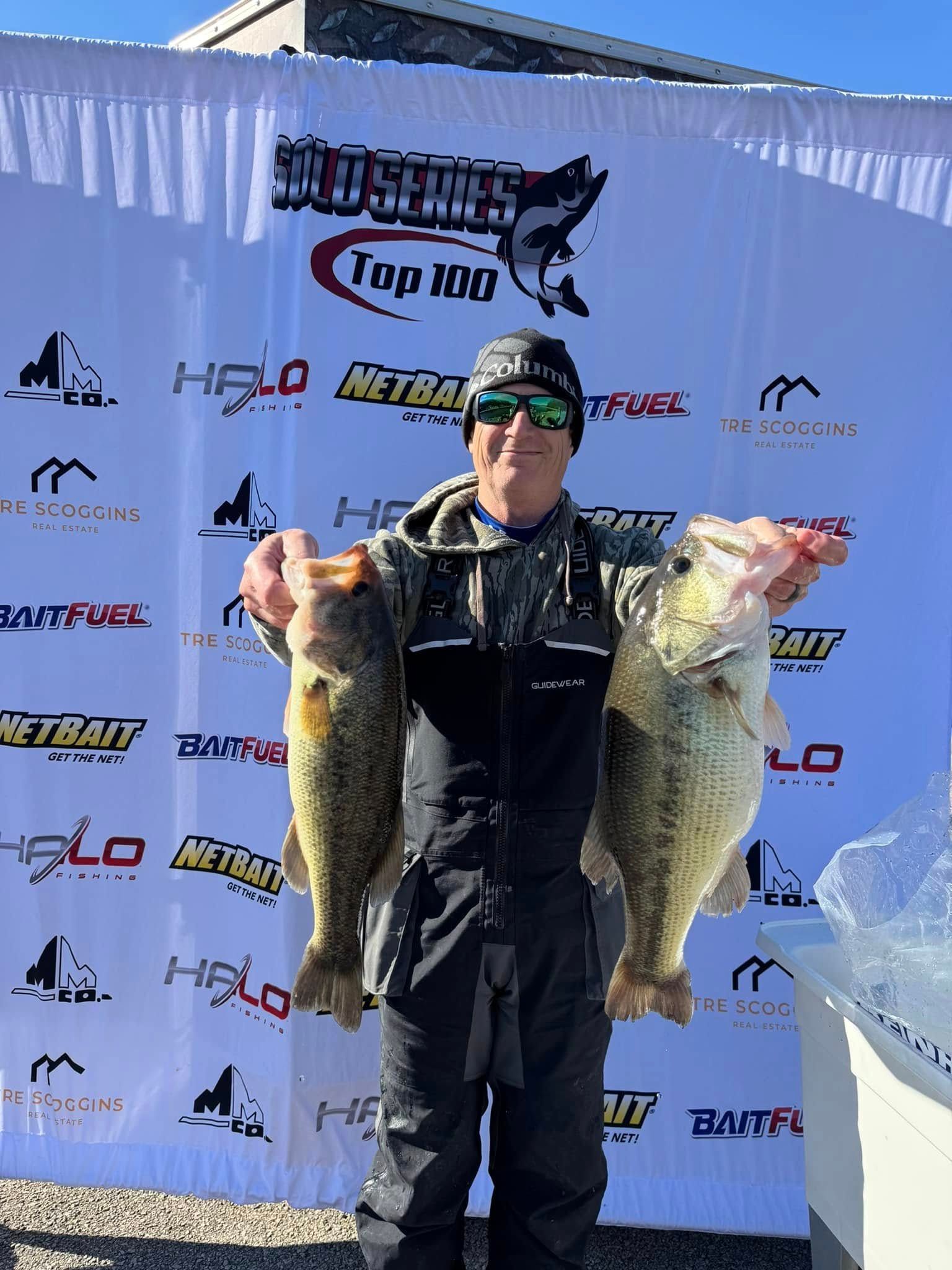 Angler posing with two large fish at an outdoor fishing tournament backdrop