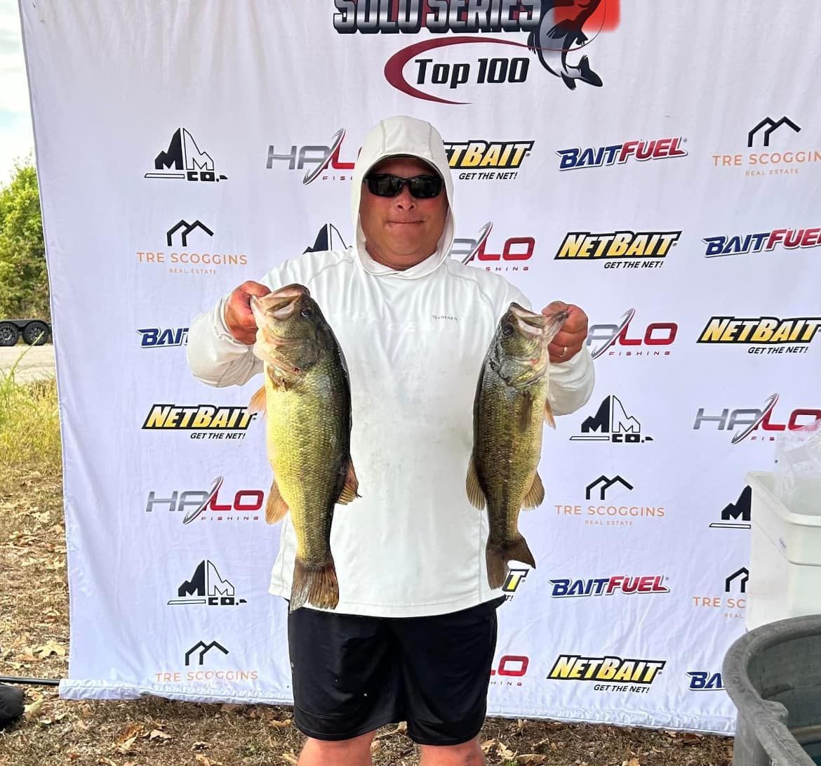 Angler holding two large fish in front of a fishing tournament sponsor backdrop
