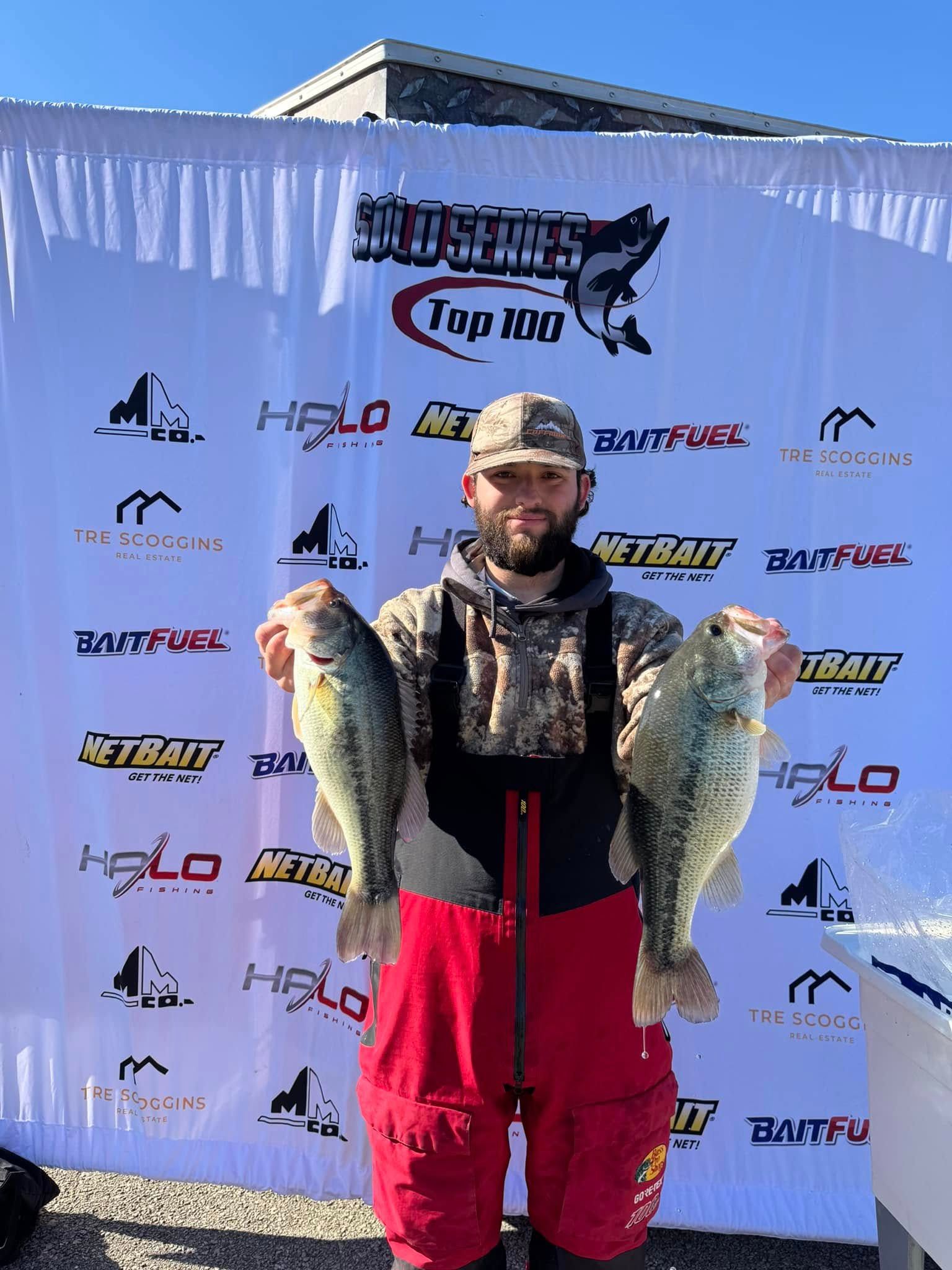 Angler holding two large fish in front of a sponsor backdrop at a fishing tournament