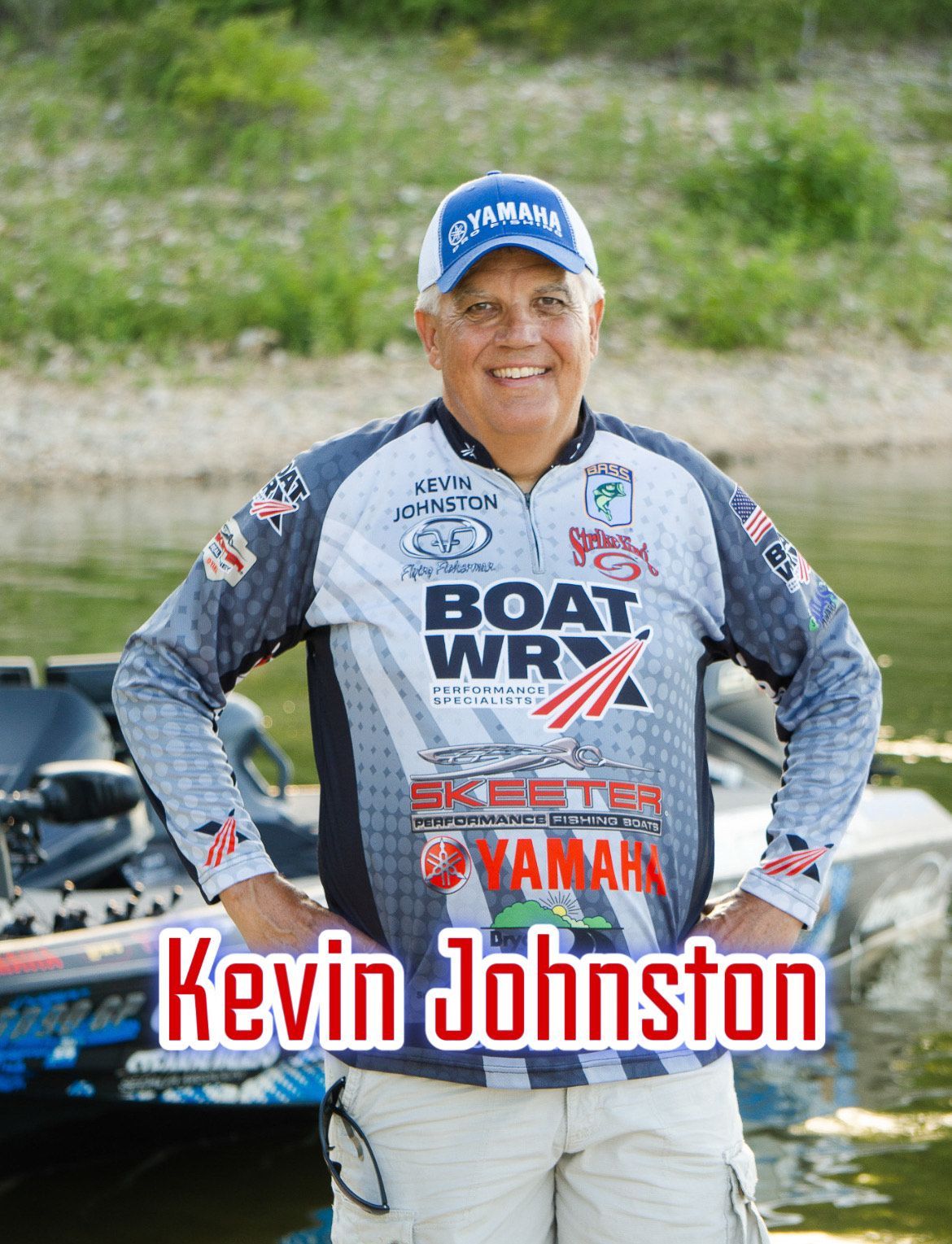 Kevin Johnston smiling in a boat racing jersey and cap, standing by the water with boats behind him.