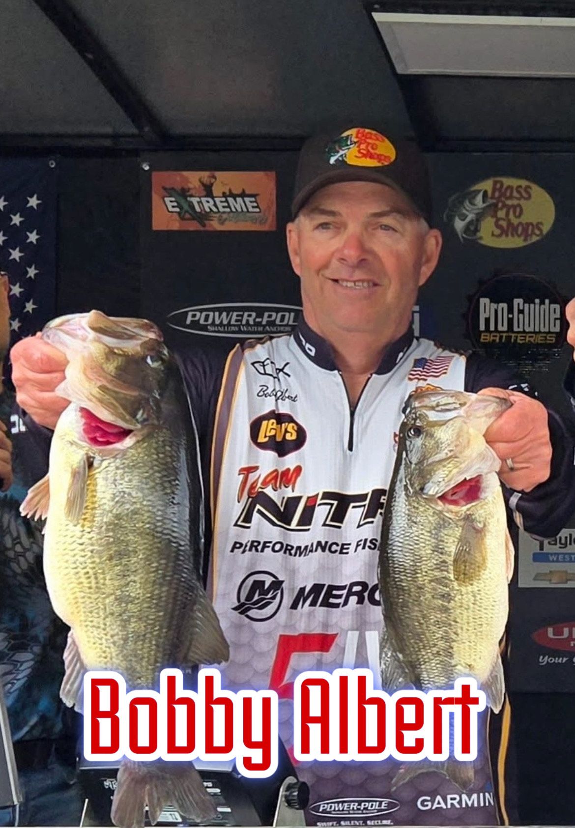 Man posing with two large fish in front of sponsor signs, with “Bobby Albert” text at bottom.