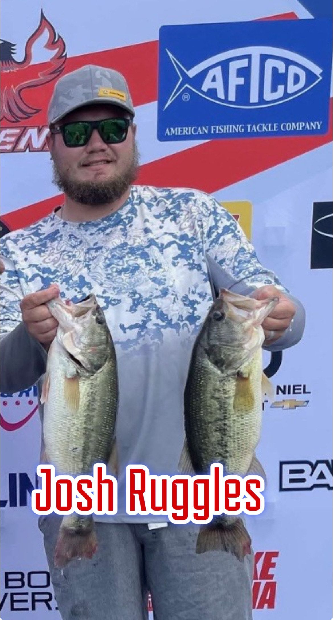 Angler holding two largemouth bass in front of an event sponsor backdrop