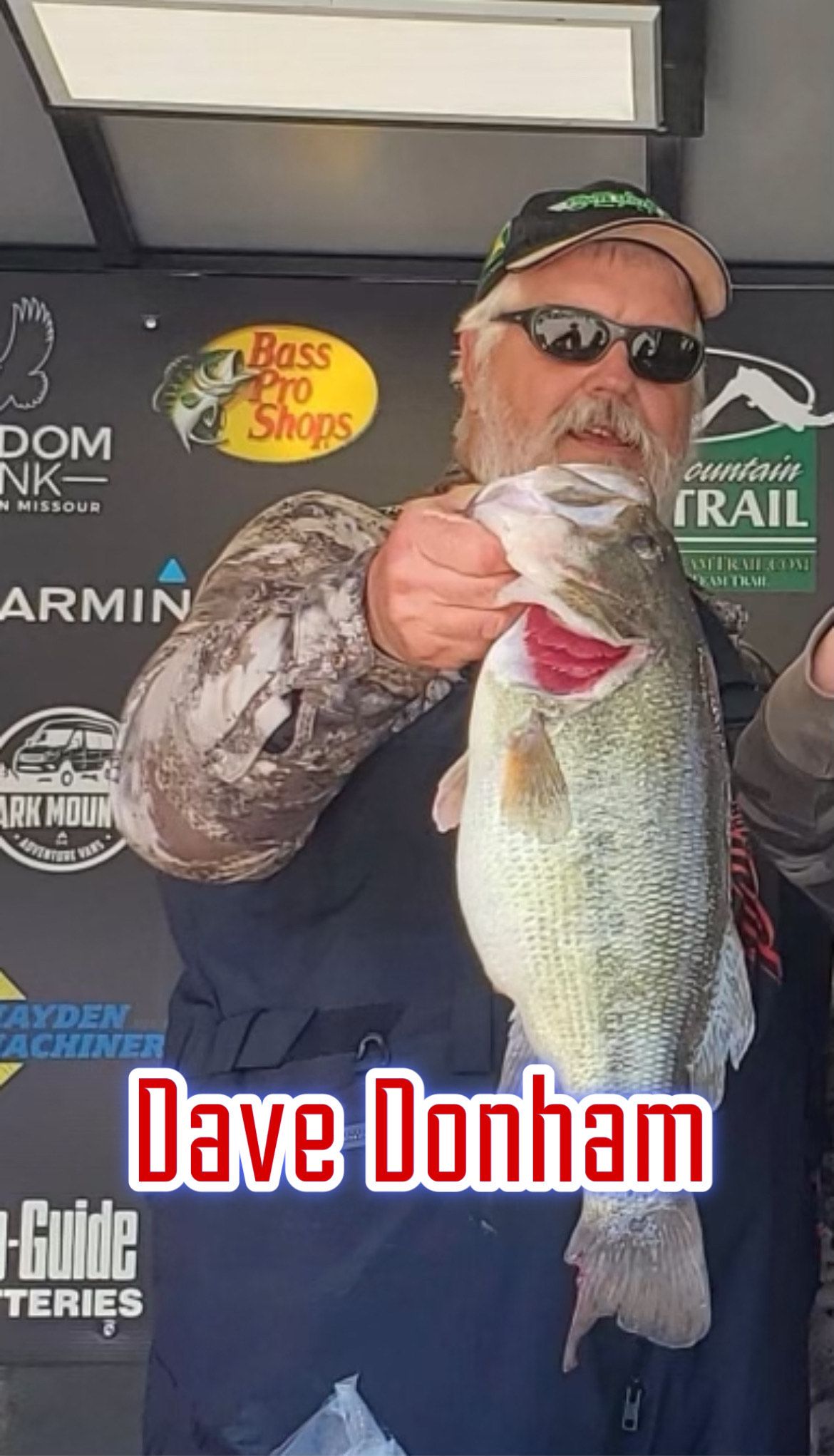 Man holding a large fish on a tournament stage, with sponsor logos and “Dave Donham” text behind him