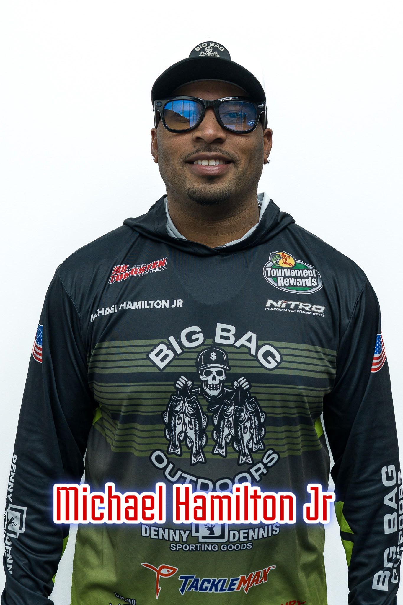 Portrait of Michael Hamilton Jr. in a black racing jersey and cap, standing against a white background.