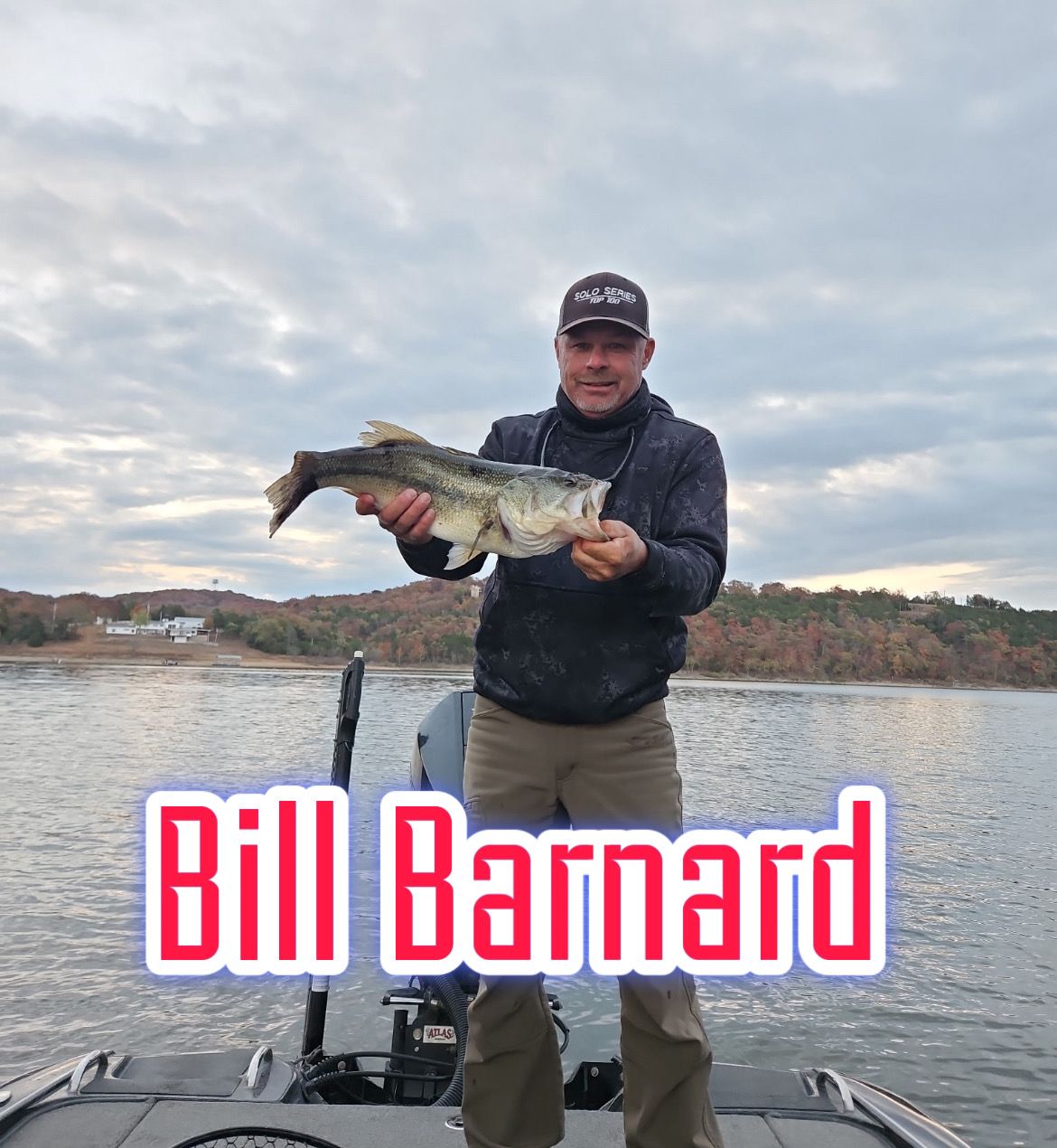Man holding a fish on a boat, with “Bill Barnard” text overlay against a lake and cloudy sky.