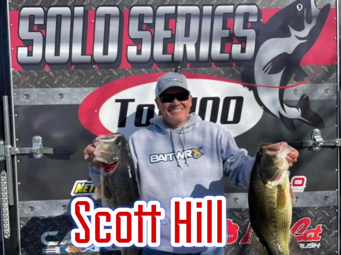 Scott Hill holding two fish in front of a Solo Series tournament banner