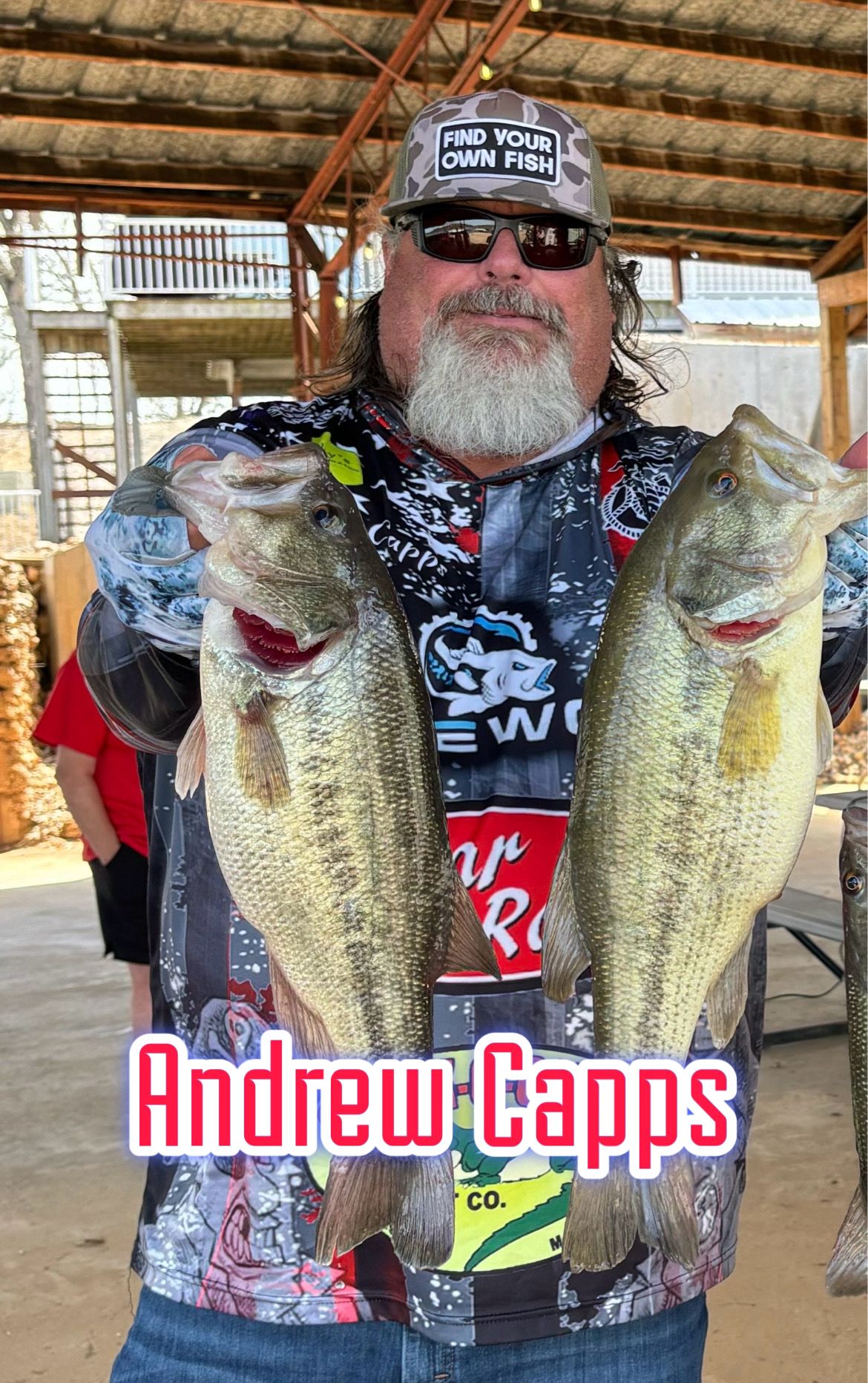 Man holding two large fish in a rustic setting, wearing a patterned shirt and sunglasses, with name text “Andrew Capps”
