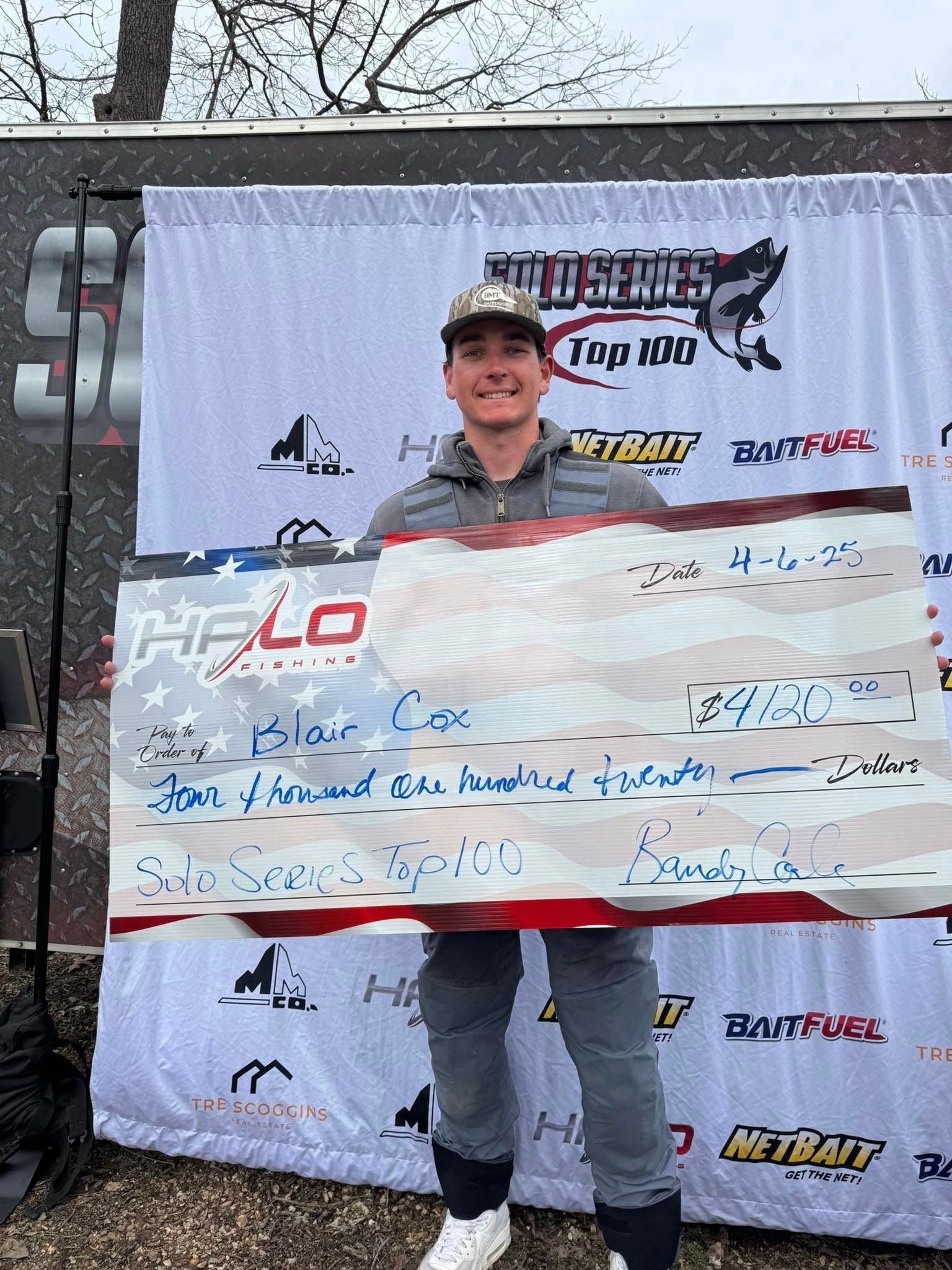 Man smiling while holding a large check at a racing event backdrop