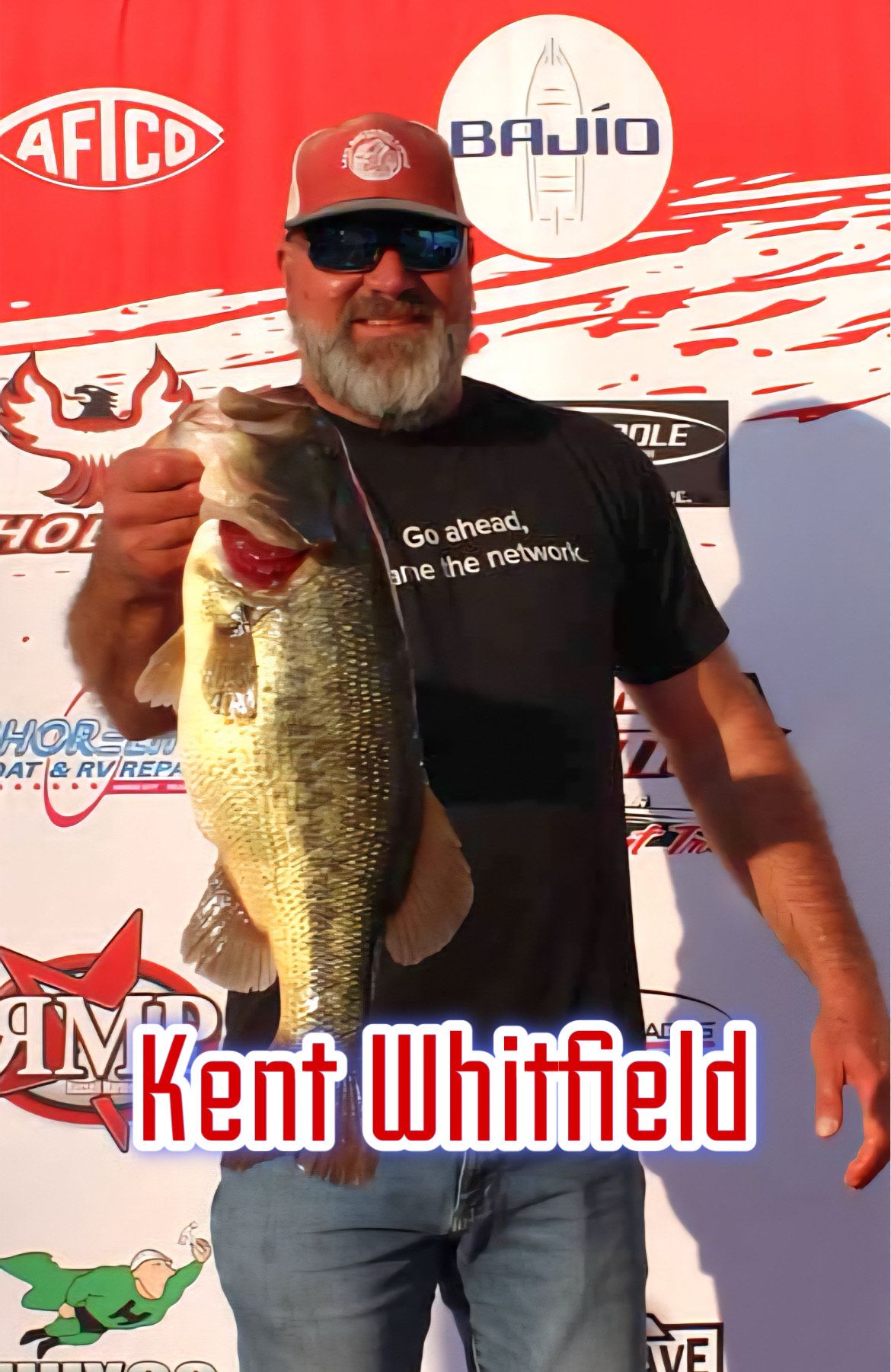 Man holding a large fish in front of sponsor banners, with “Kent Whitfield” text at bottom