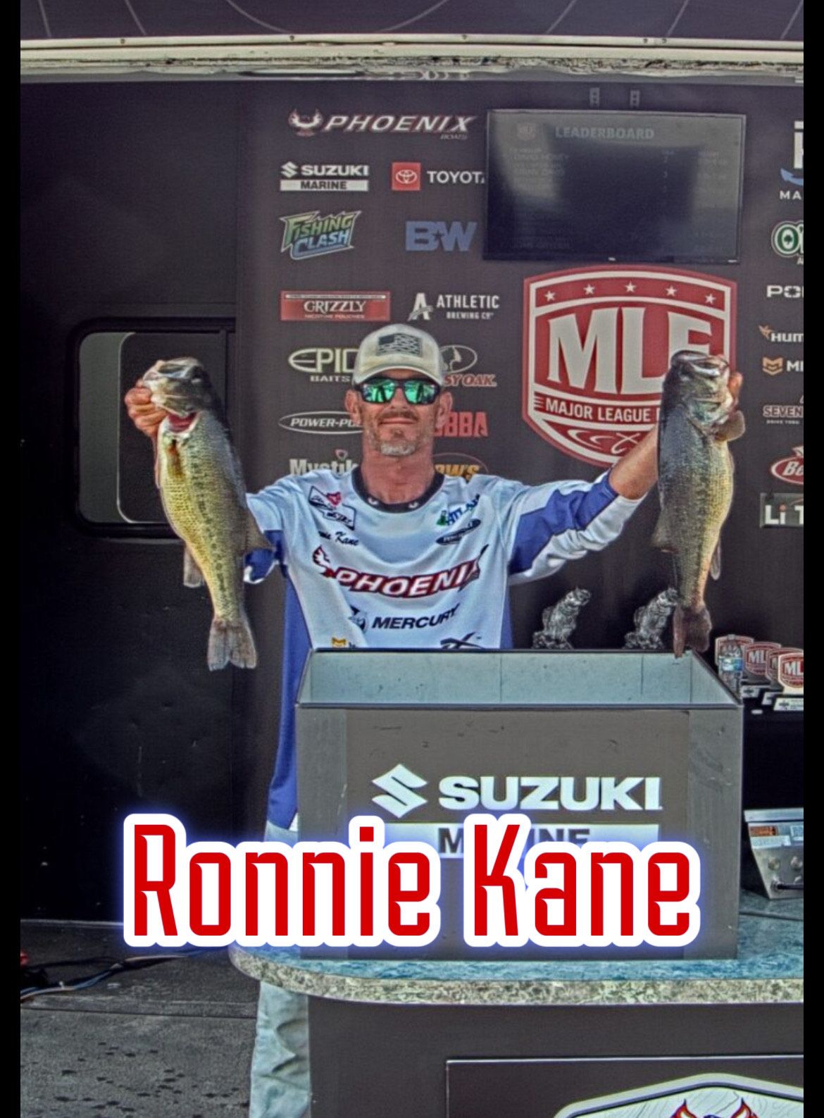 Ronnie Kane holding two fish on a Suzuki podium at an MLF fishing event