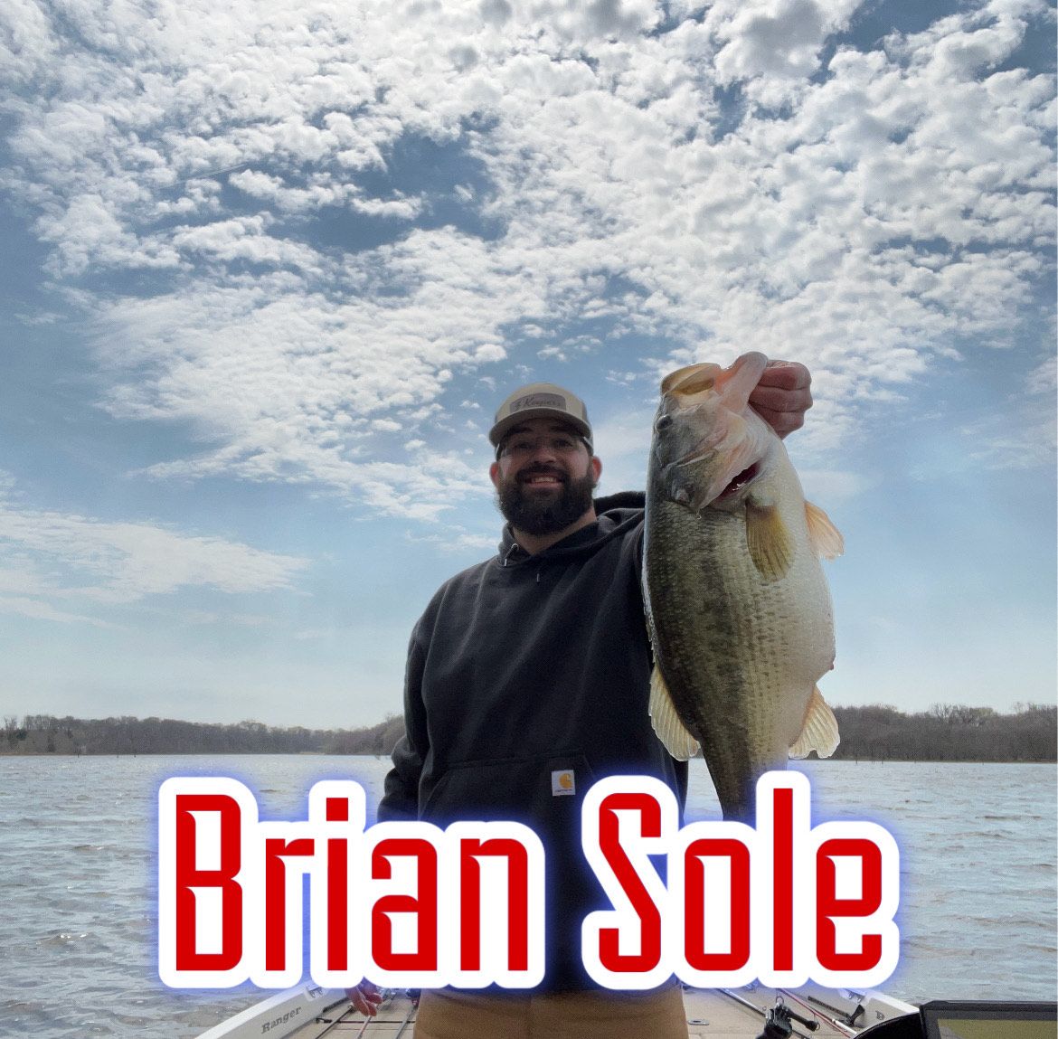 Man holding a large fish by a lake under a cloudy sky, with “Brian Sole” text at the bottom