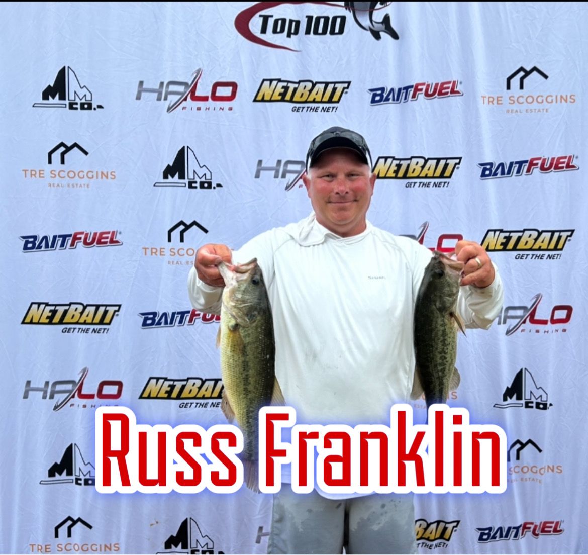 Russ Franklin holding two large fish in front of sponsor banners at a fishing event