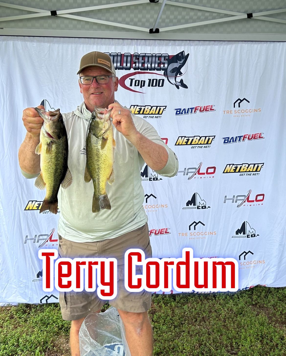Man holding two bass fish at a fishing tournament backdrop with the name Terry Cordum
