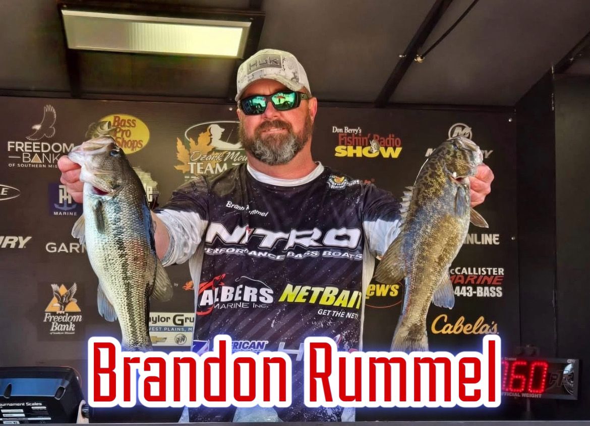 Man holding two fish in front of sponsor backdrop, with “Brandon Rummel” text at bottom