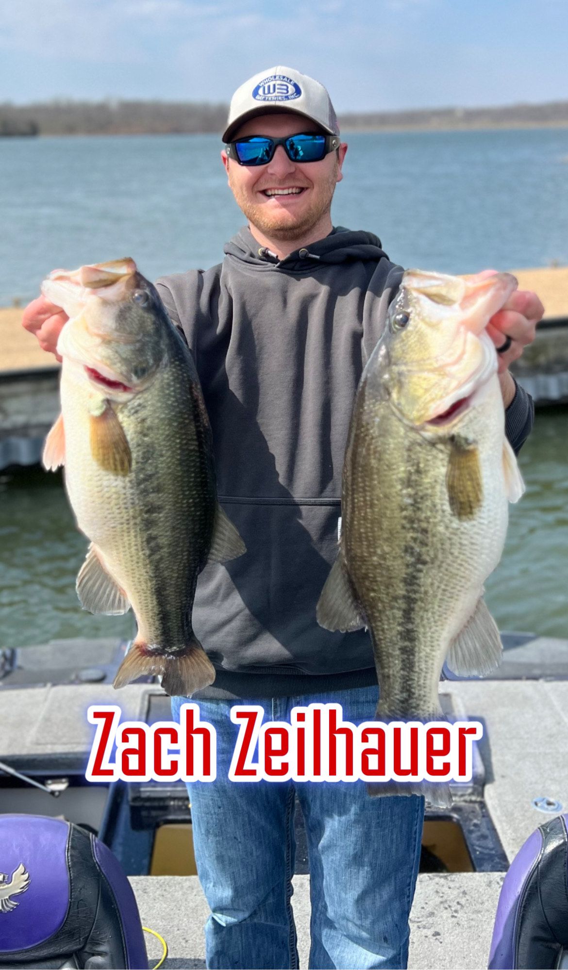 Man smiling on a boat holding two large fish, with “Zach Zeilbauer” text at the bottom.