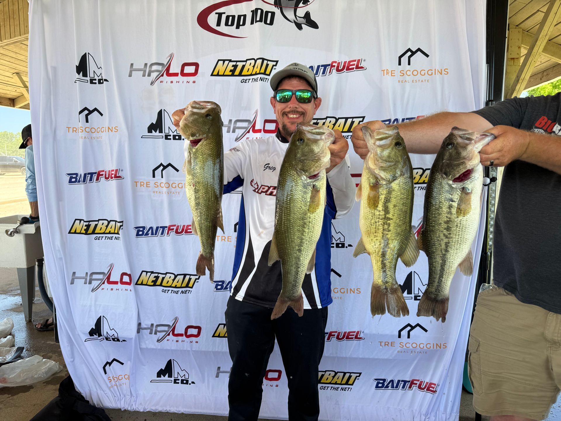 Man holding three large fish in front of a branded tournament backdrop.