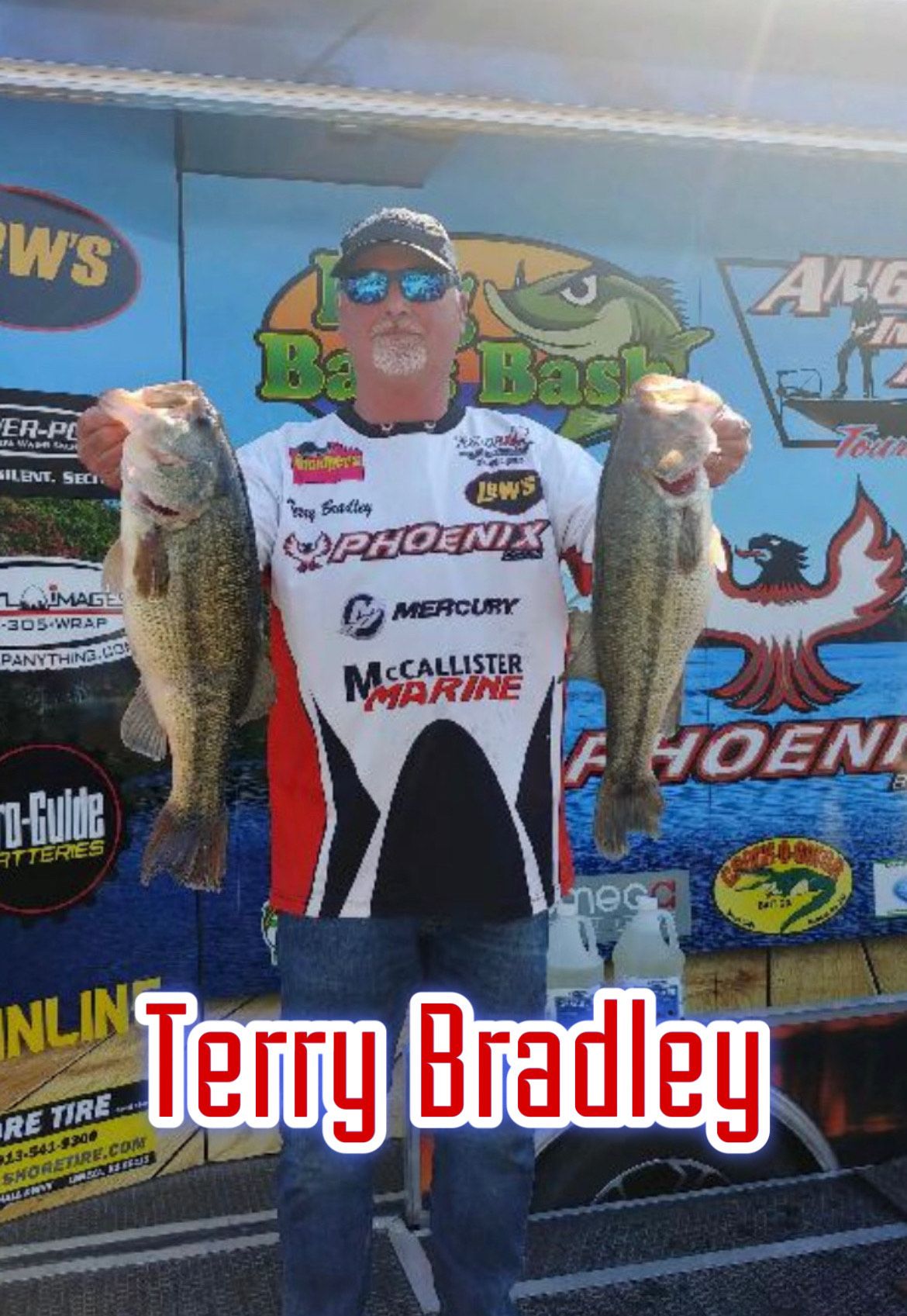 Terry Bradley holds two fish in front of sponsor logos, wearing a white and black fishing jersey.