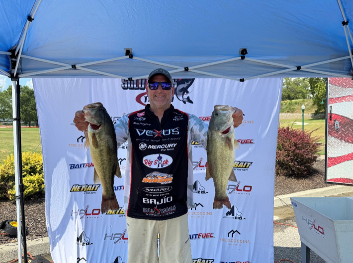 Angler holding two large fish under a blue tent at a fishing tournament