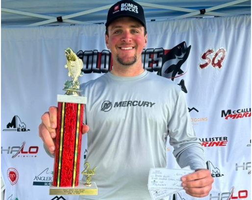 Smiling man holding a trophy and ticket at an outdoor event booth
