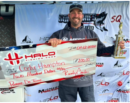 Man smiling and holding a large novelty check and trophy at a racing event backdrop