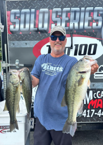 Angler smiling and holding two large bass in front of a Solo Series 1100 banner