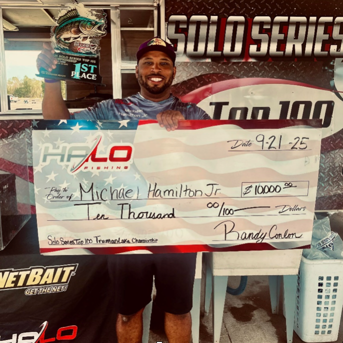 Man holding a $10,000 check at a fishing tournament booth, smiling in front of a Solo Series banner.