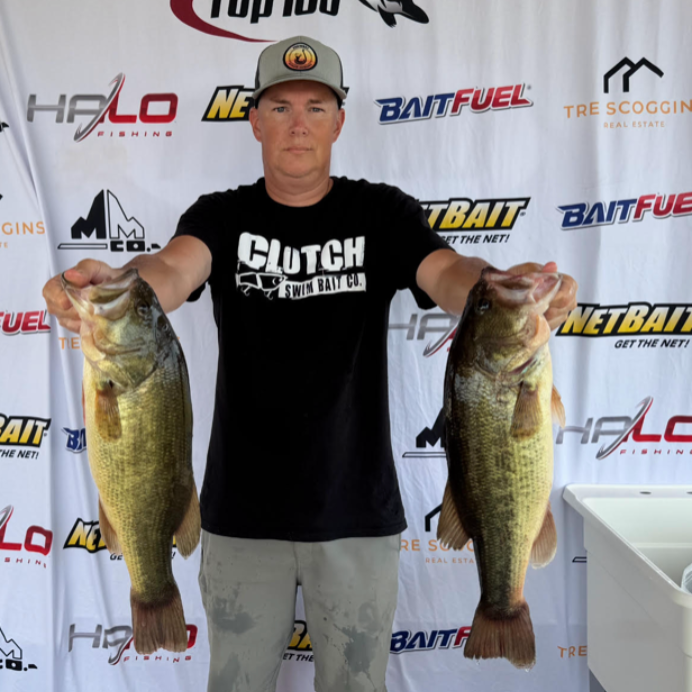 Man holding two large bass fish in front of a sponsor logo backdrop