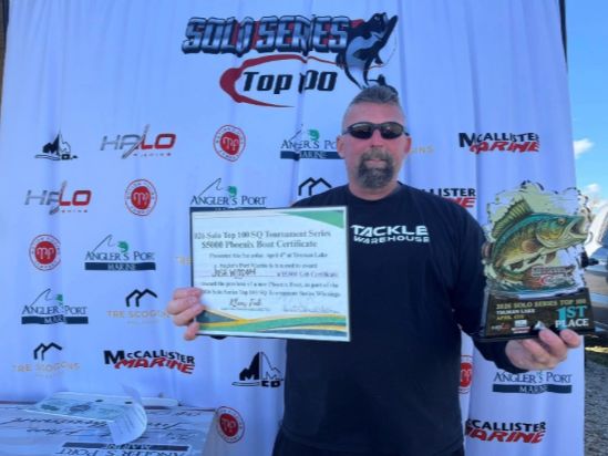 Man holding a certificate and trophy in front of a sponsor backdrop at an awards event