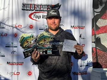 Man holding trophy and certificate in front of sponsor backdrop at a fishing competition