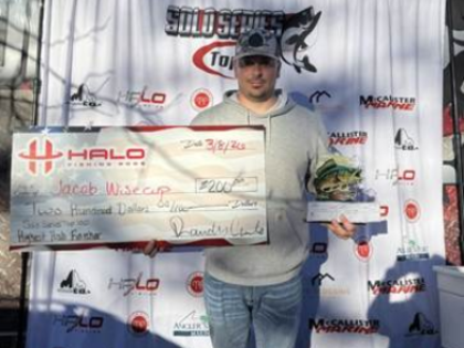 Man holding a large check on a stage backdrop at a racing event