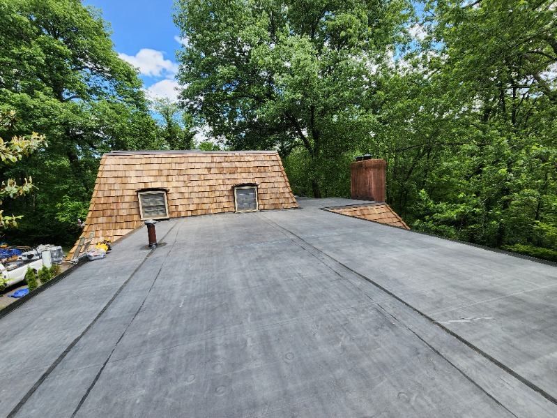 A roof with a chimney on it is surrounded by trees.
