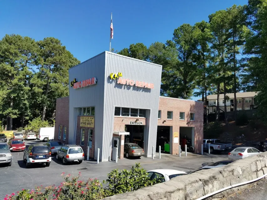 Small commercial building with storefronts, parked cars, and trees on a sunny street.