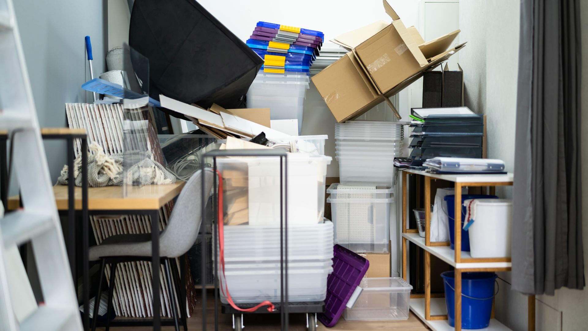 Cluttered home office with stacked papers, boxes, shelves, and a chair tucked beside a desk