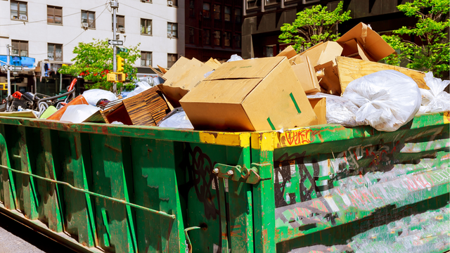 Green dumpster overflowing with cardboard boxes and trash on a city street