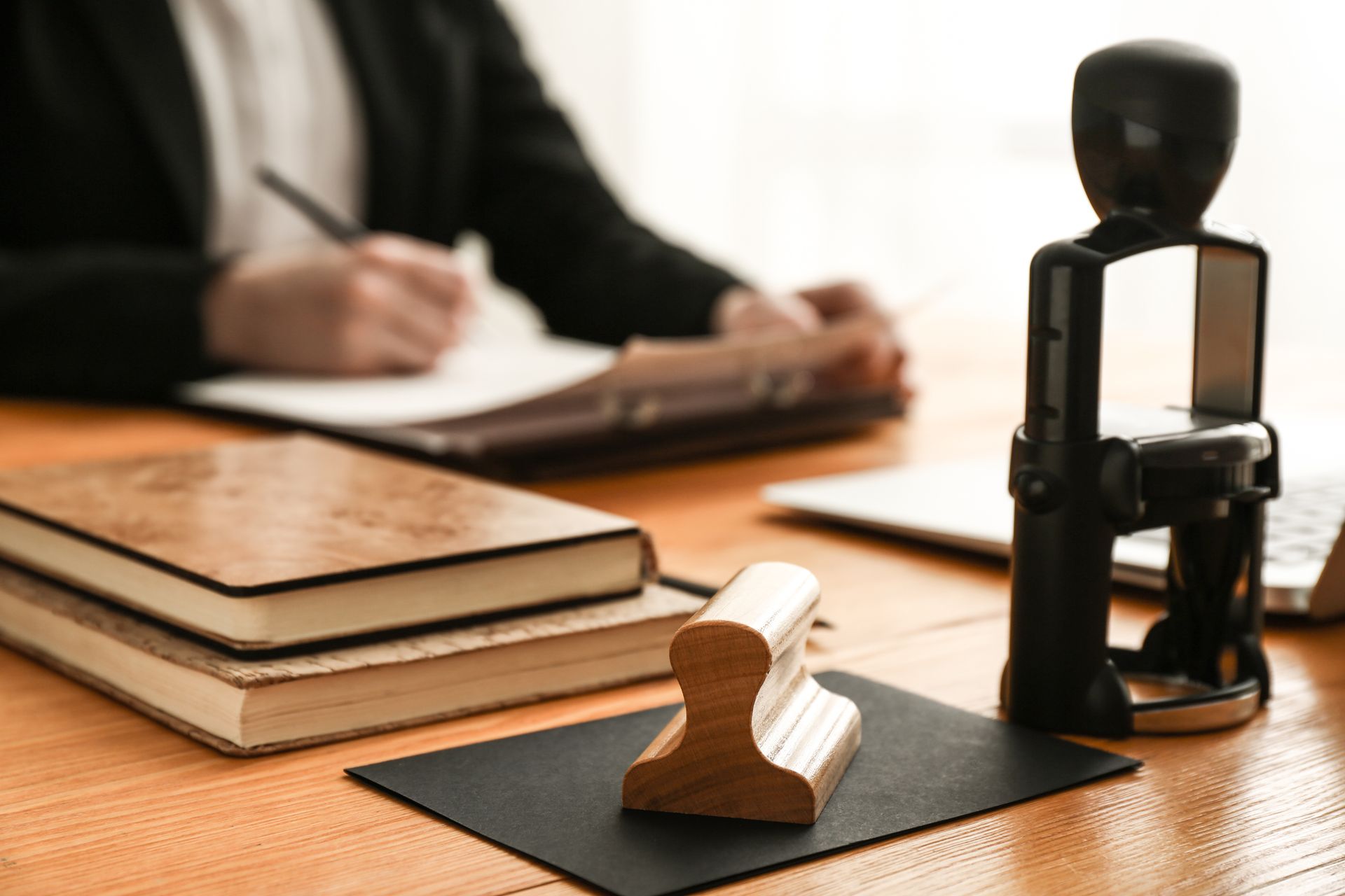 Wooden stamp on ink pad, stack of books, person writing at desk.
