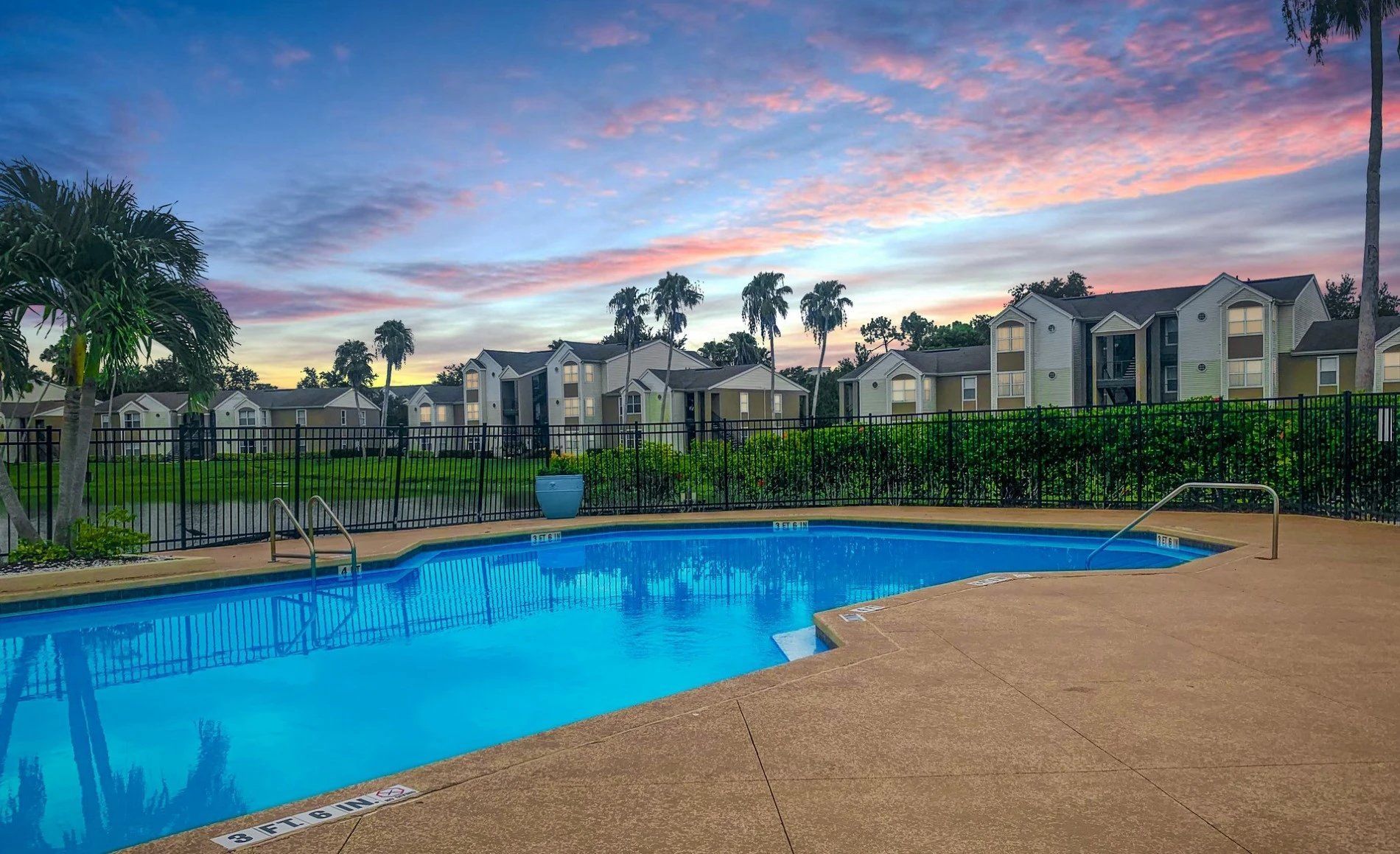 Pool at sunset with apartment buildings in the background; blue water and pink and purple sky.