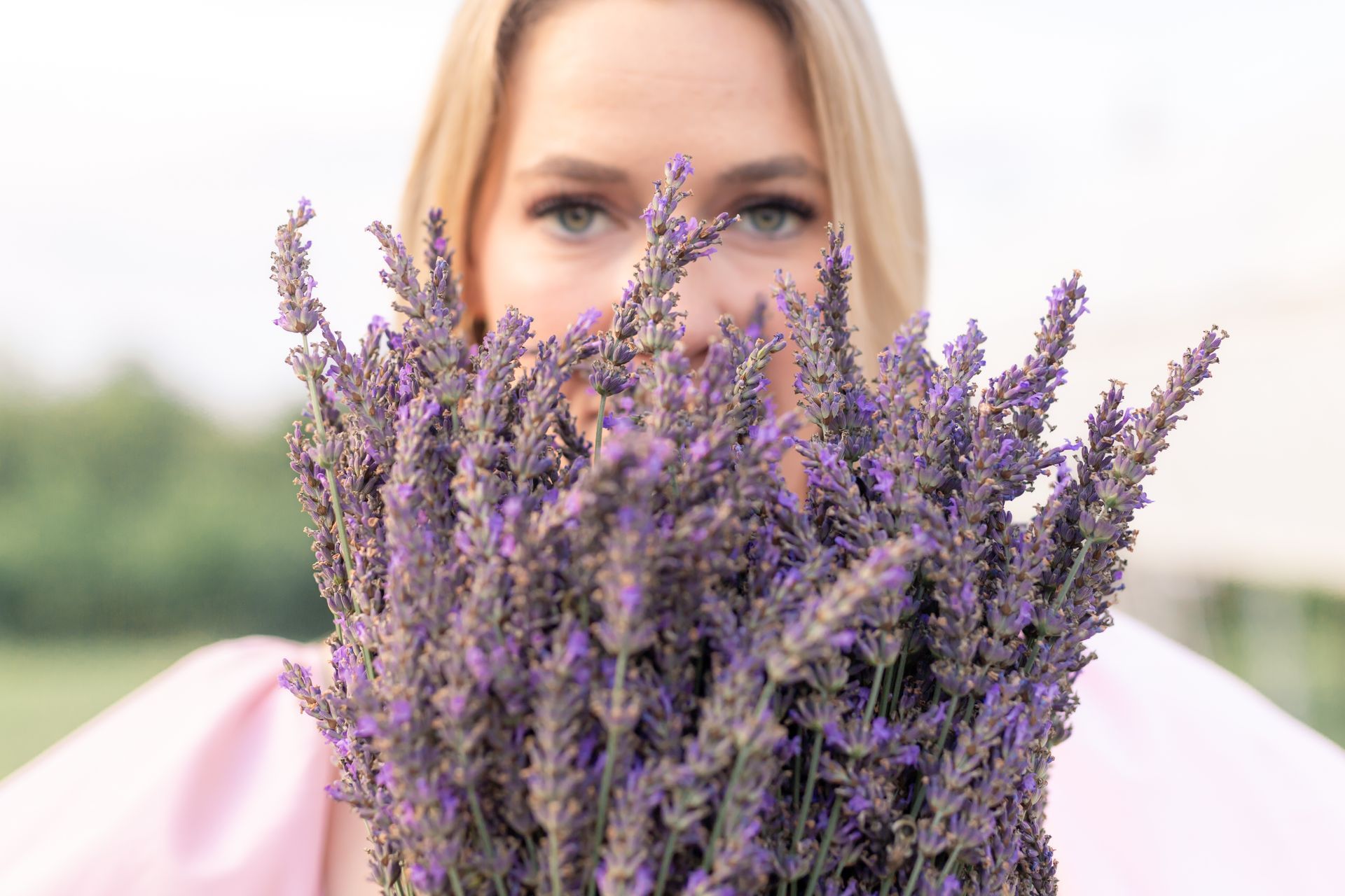 A woman is holding a bouquet of lavender flowers in front of her face.