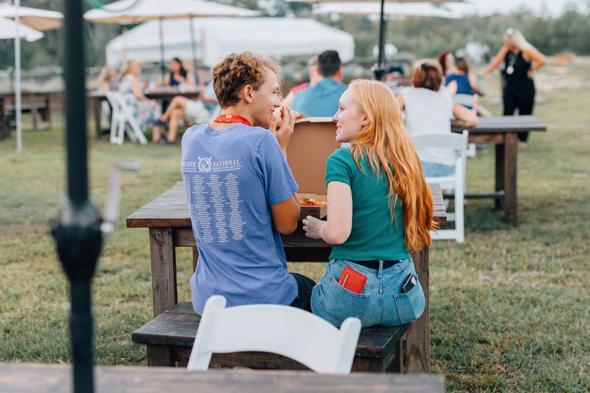 A man and a woman are sitting at a picnic table eating pizza.