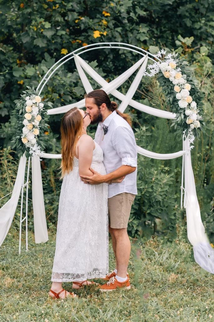 A man and a woman are kissing in front of a white arch.